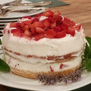 2 layer strawberry shortcake with a big pikle of strawberries on top and and fresh greens decorating the sides