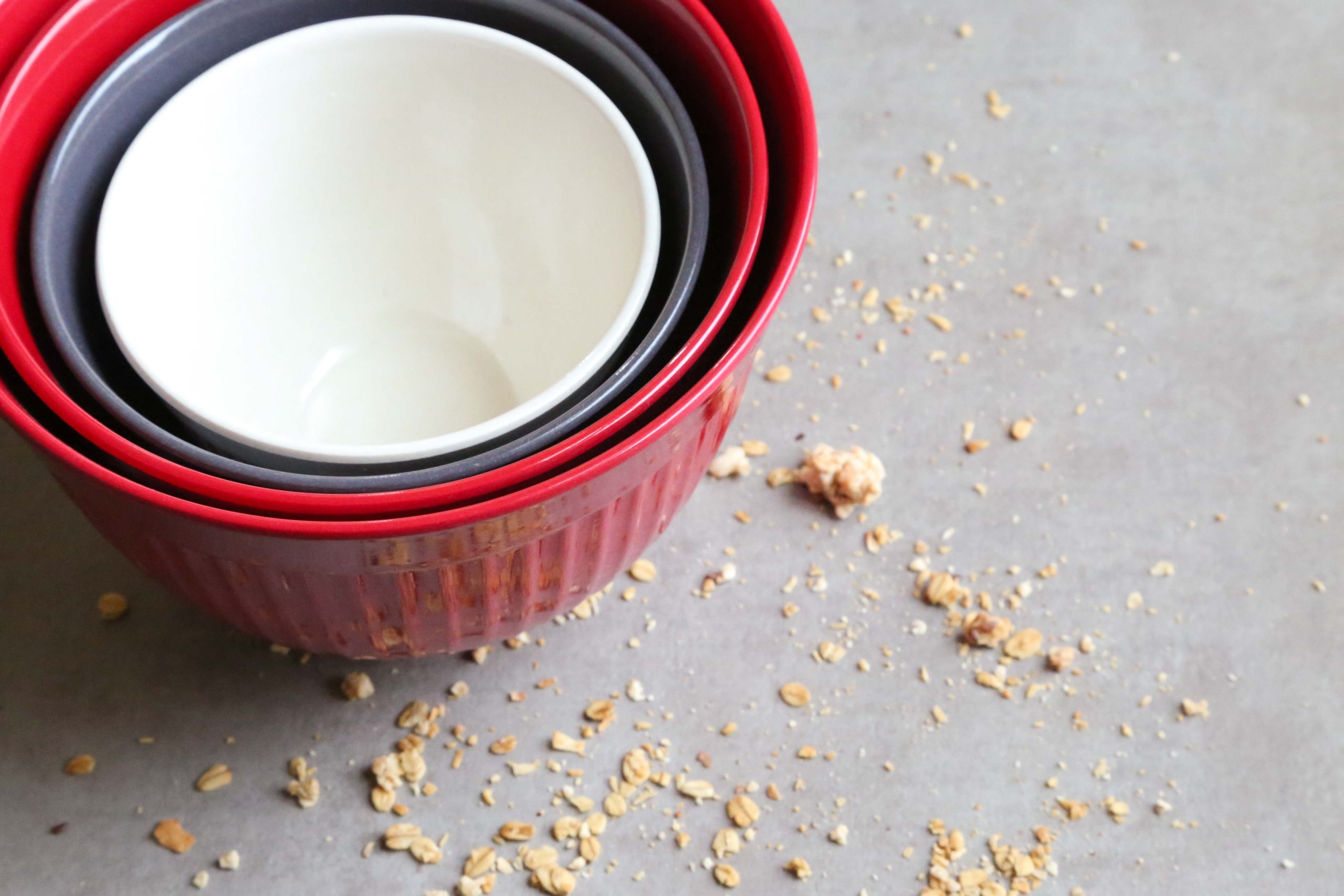 3 stacked bowls in while, blue, and red sitting on a table scattered with crumbs